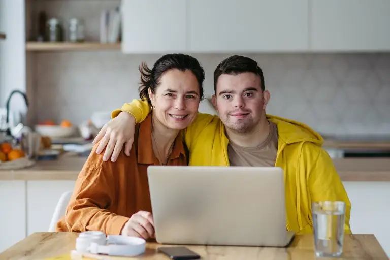 An image of a mom teaching a young man on how to use a laptop, captured by Your Best Life Independent Living.